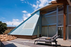 A modern building with a unique triangular facade, large windows, and a pool area with lounge chairs. - Casas Bioclimáticas Iter El Cangrejo (Granadilla de Abona)