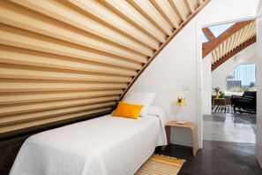 A bedroom with a sloped ceiling, a bed with white bedding and a yellow pillow, a bedside table with a lamp, and a view of the outdoors. - Casas Bioclimáticas Iter El Cangrejo (Granadilla de Abona)