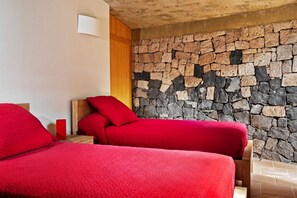 Ein Zimmer mit zwei Betten, jeweils mit roter Bettwäsche, einer Steinwand und einer Holzbalkendecke.