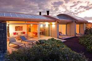 Ein modernes Haus mit Solaranlage, einer Terrasse mit Liegestühlen und einem Garten.
