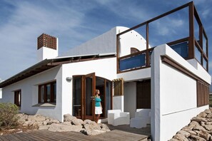 A modern two-story house with a wooden deck, large windows, and a stone wall. - Casas Bioclimáticas Iter La Arcilla (Granadilla de Abona)