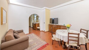 Sala de estar com sofá, área de jantar com mesa e cadeiras, televisão e corredor que dá para outro quarto.