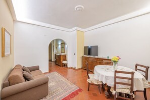 A living room with a sofa, a dining area with a table and chairs, a TV, and a hallway leading to another room. - 4BNB - Domus Battistini (Rome)