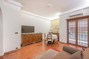 Een woonkamer met een televisie, een houten kast, een eettafel, stoelen en een kamerbreed tapijt met een patroon.