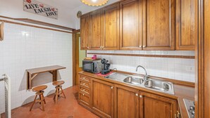 Uma cozinha com armários de madeira, pia, micro-ondas e uma pequena mesa com banquetas.