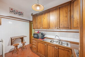 A kitchen with wooden cabinets, a sink, a microwave, and a small table with stools. - 4BNB - Domus Battistini (Rome)