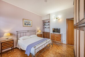 A bedroom with a bed, bedside tables, a TV, a dresser, and a shelf unit. - 4BNB - Domus Battistini (Rome)