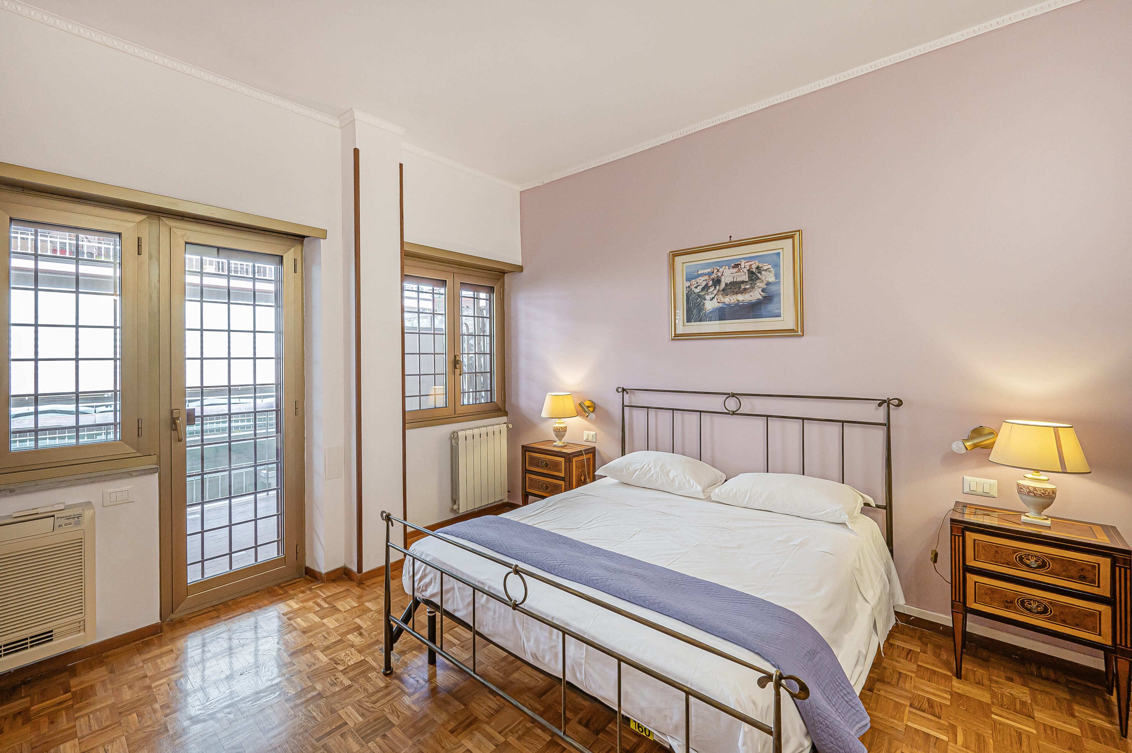 Ein Schlafzimmer mit einem Bett, zwei Nachttischen, einer Heizung und zwei Fenstern.