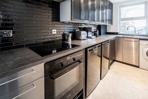 A modern kitchen with stainless steel appliances, a black tiled backsplash, and a window providing natural light. - Luxury flat in Notting Hill, 4 mins Portobello Market. 3 large double beds. (London)