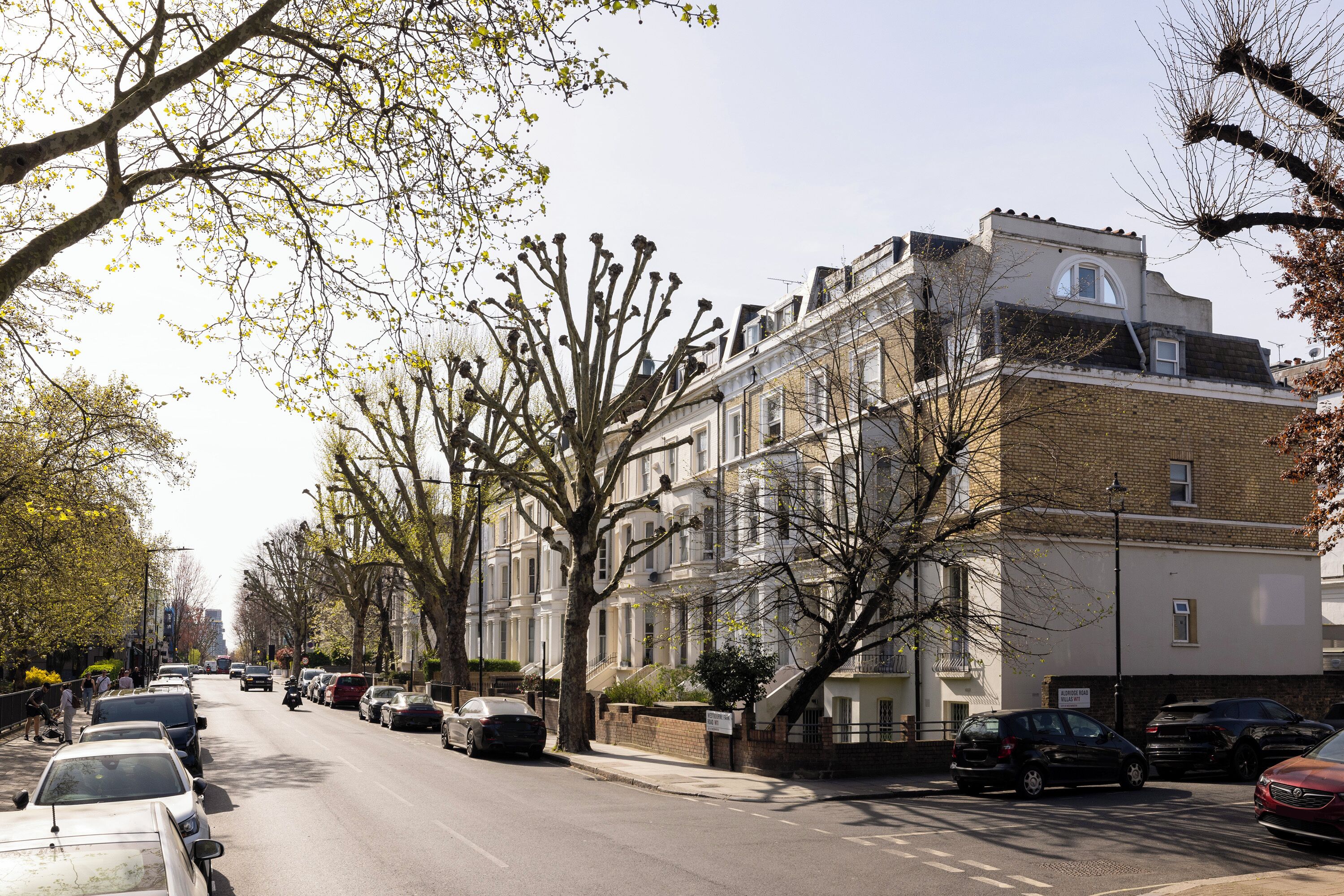 A street lined with multi-story buildings, parked cars, and leafless trees.