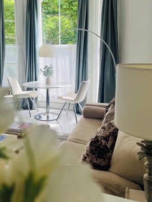 A modern living room with a round glass table, two white chairs, a beige sofa with a patterned pillow, and a floor lamp. - Luxury flat in Notting Hill, 4 mins Portobello Market. 3 large double beds. (London)