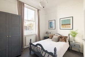 A bedroom with a bed, a nightstand, a dresser, a window with curtains, and two framed pictures on the wall. - Luxury flat in Notting Hill, 4 mins Portobello Market. 3 large double beds. (London)