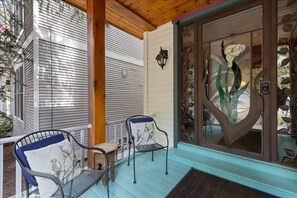 Varanda com duas cadeiras e uma mesa, teto de madeira e porta de vidro decorada com motivos florais.