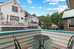 Un balcón con mesa y sillas, con vista a una zona residencial con casas y árboles.