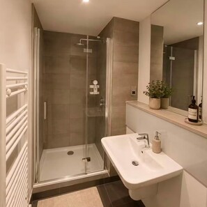 A modern bathroom with a glass-enclosed shower, a white sink, and a mirror above the sink. - Salford Serenity - Modern 2 Bedroom Apartment (Salford)