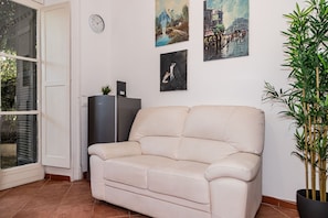 A living room with a beige sofa, a black cabinet, and a wall clock. There are three paintings on the wall. - Aurelia Vatican Home (Roma)