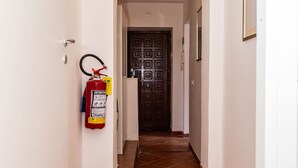 A hallway with a fire extinguisher mounted on the wall, a tiled floor, and a door at the end. - Aurelia Vatican Home (Roma)