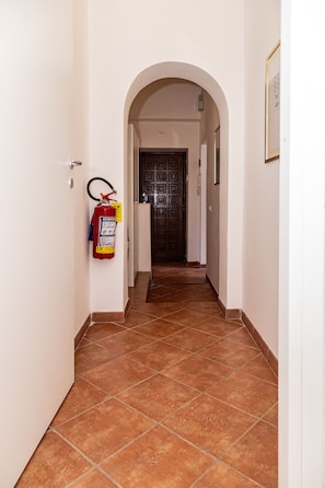 A hallway with a fire extinguisher mounted on the wall, a tiled floor, and a door at the end. - Aurelia Vatican Home (Roma)