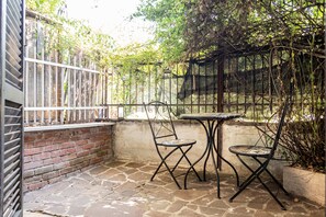 A patio with a brick wall, a metal fence, and a table with chairs. - Aurelia Vatican Home (Roma)