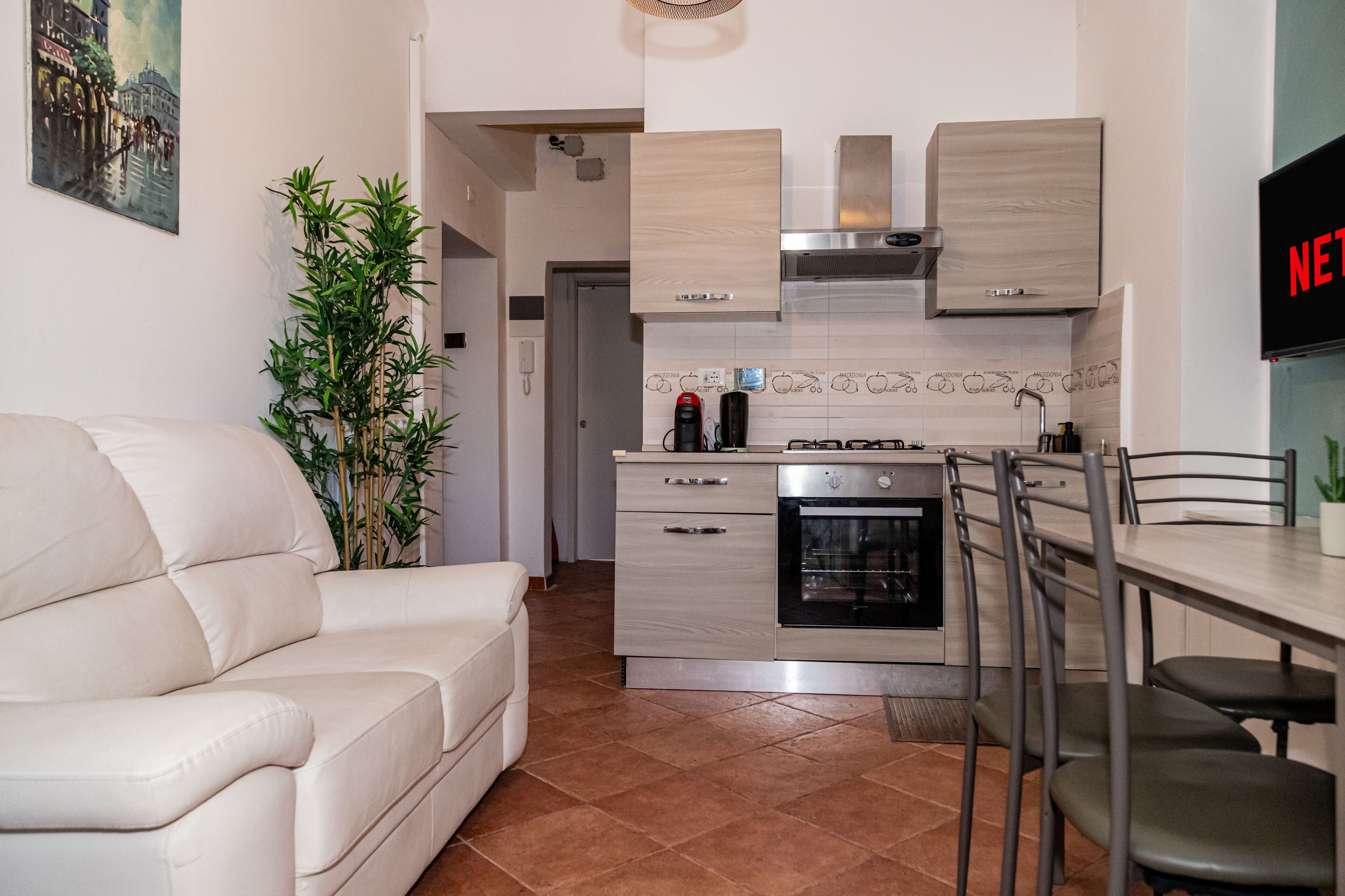 Eine moderne Küche mit Einbauofen, ein Essbereich mit Tisch und Stühlen sowie ein Wohnzimmer mit Sofa und Topfpflanze.