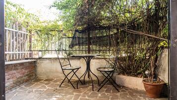 Eine Terrasse mit Steinboden, zwei Metallstühlen, einem kleinen runden Tisch und einem Blumentopf.