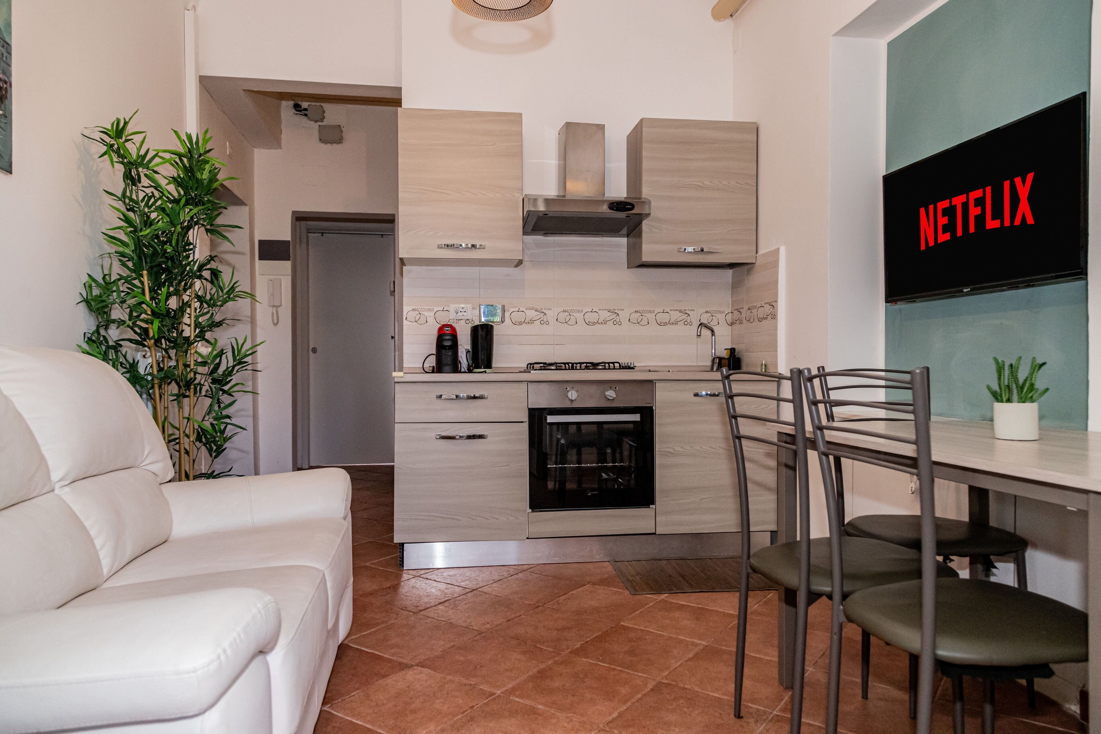 Una cuina moderna amb forn integrat, zona de menjador amb taula i cadires, i saló amb sofà.