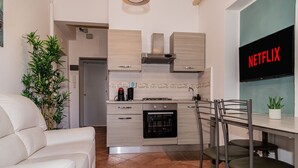 A modern kitchen with a built-in oven, a dining area with a table and chairs, and a living room with a sofa. - Aurelia Vatican Home (Roma)