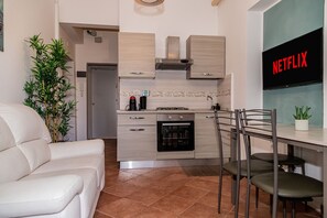 A modern kitchen with a built-in oven, a dining area with a table and chairs, and a living room with a sofa. - Aurelia Vatican Home (Roma)
