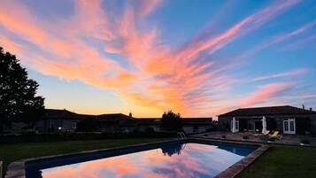 A swimming pool with a clear view of the sky during sunset, surrounded by a residential area with houses and a patio.