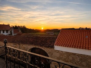 Ein Sonnenuntergang über einem Dach mit Terrakotta-Ziegeln, Steinmauern und einem Balkongeländer.