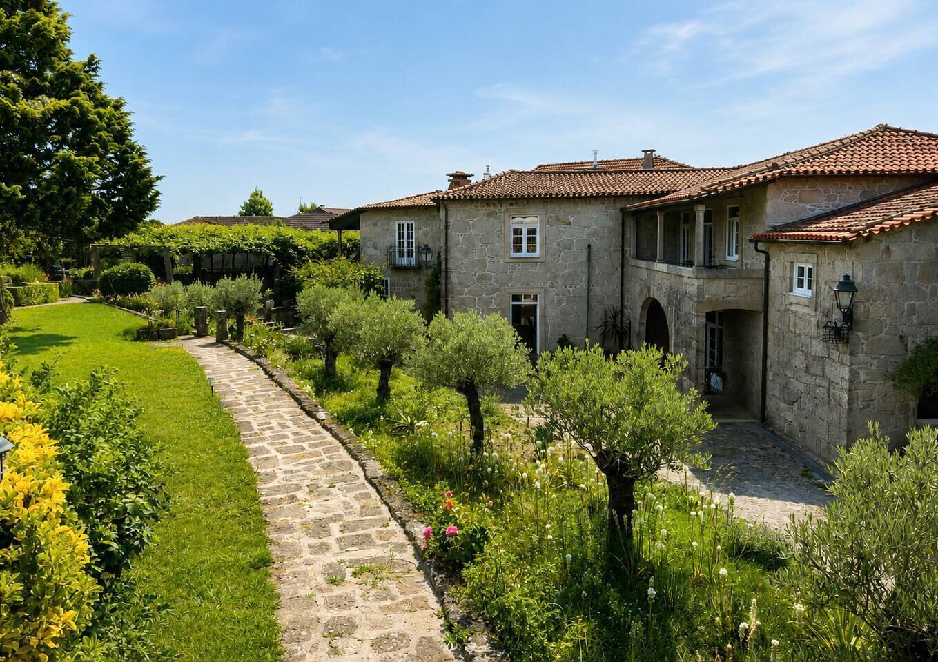 A stone building with a tiled roof, a paved pathway, and lush greenery.