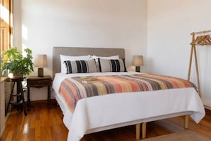 Ein Schlafzimmer mit einem Bett, Nachttischen, Lampen, einer Pflanze und Holzboden.