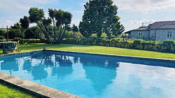 A rectangular swimming pool with a clear blue water surface, surrounded by a well-maintained grassy area and a variety of trees.