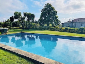 Ein rechteckiger Pool mit klar blauem Wasser, umgeben von einer gepflegten Rasenfläche und verschiedenen Bäumen.