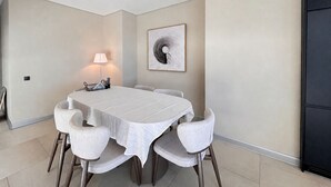 Een eethoek met een ronde tafel, zes stoelen, een lamp en een kunstwerk aan de muur.