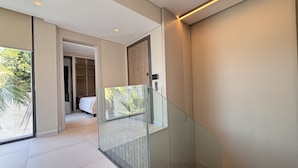 Een modern interieur met een glazen trap, een slaapkamer met een bed en uitzicht op groen buiten.