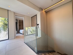 Ein modernes Interieur mit einer Glasstufenwendeltreppe, einem Schlafzimmer mit Bett und Blick ins Grüne.