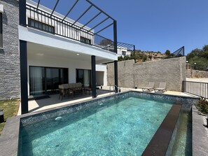 Ein modernes, zweistöckiges Haus mit Swimmingpool, Gartenmöbeln und einer Steinmauer.