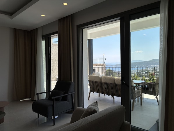 A modern room with a sofa, armchair, and a balcony with a view of the sea.
