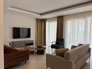 Ein modernes Wohnzimmer mit Flachbildfernseher, einer Couch, einem Sessel und einem Couchtisch.