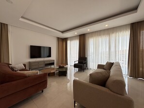 A modern living room with a flat-screen TV, a sofa, a chair, and a coffee table. - Elegant Türkbükü Retreat | Private Pool (Bodrum)