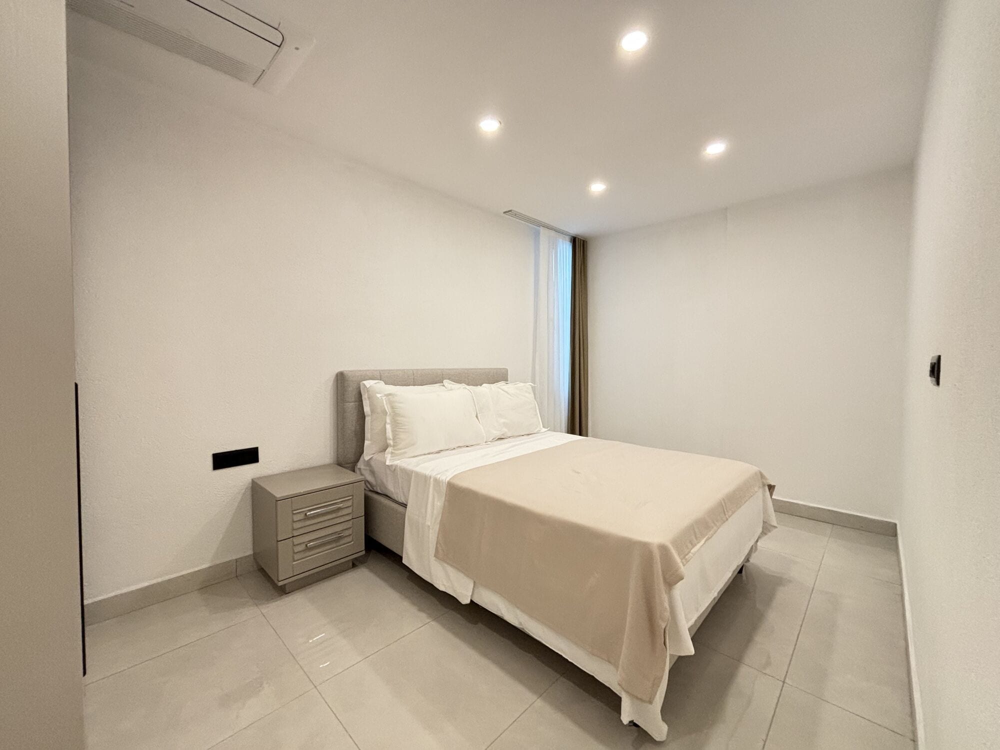 A bedroom with a bed, bedside table, and a window with curtains.