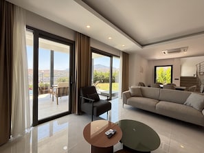 A spacious living room with a sofa, a chair, a coffee table, and large windows offering a view of the outdoors.