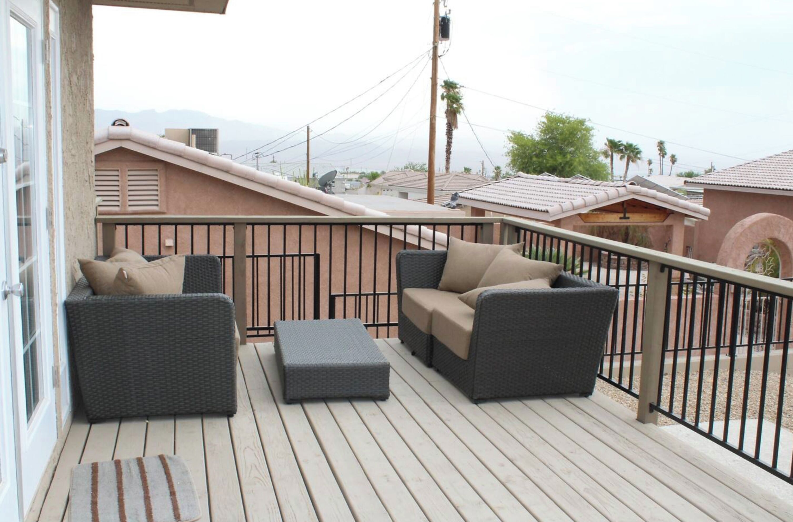 Un balcon agrémenté de deux canapés en osier gris, d’un canapé beige et d’un pouf assorti.