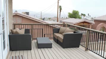 Ein Balkon mit zwei grauen Korbsesseln, einem beigen Sofa und passendem Hocker.