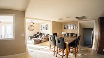A dining area with a table and chairs, a ceiling fan, and a view of the living room.