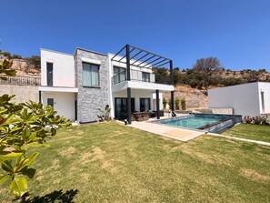 A modern two-story house with a swimming pool, a covered patio, and a stone wall.