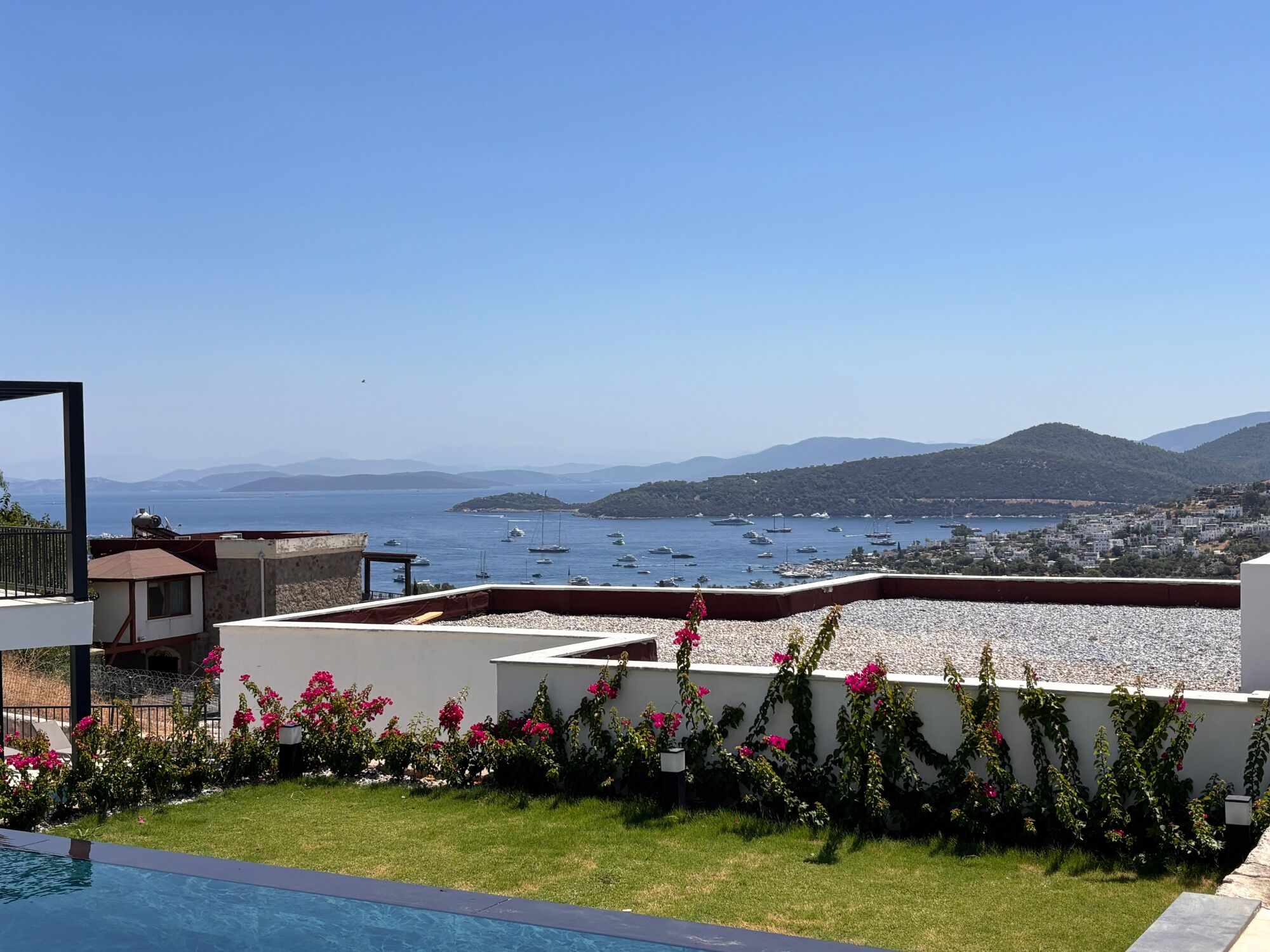 A poolside view overlooking a coastal area with boats and a town in the distance.