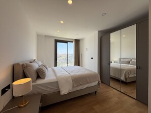 A modern bedroom with a bed, bedside lamp, and a view through a large window.
