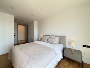 A modern bedroom with a large bed, a bedside table with a lamp, and a door leading to another room. - Private Pool Villa for Groups | Türkbükü (Bodrum)